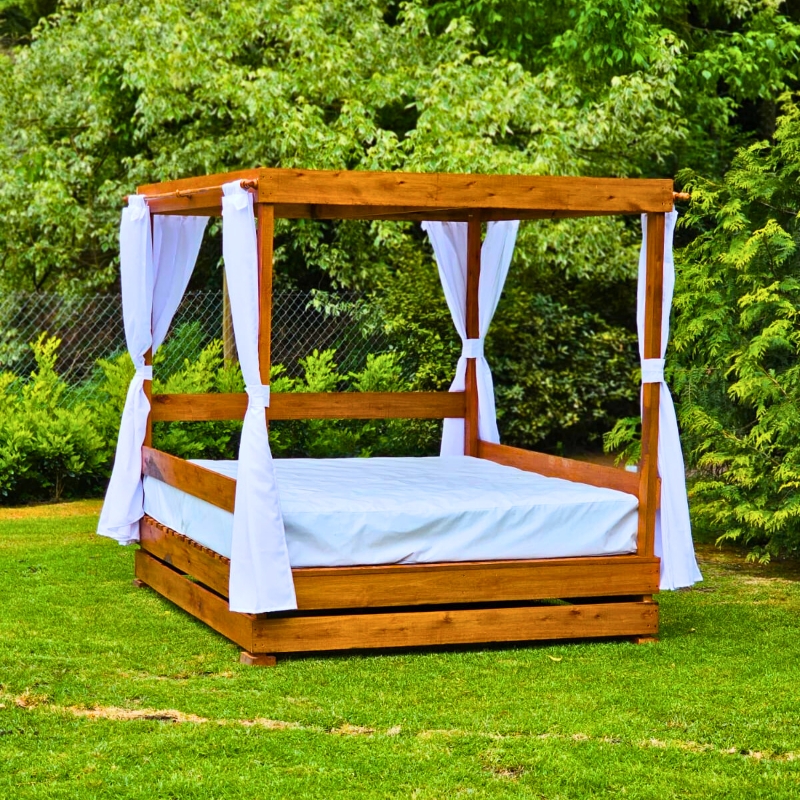 Pérgola de madera con cortinas blancas y colchón sobre el césped