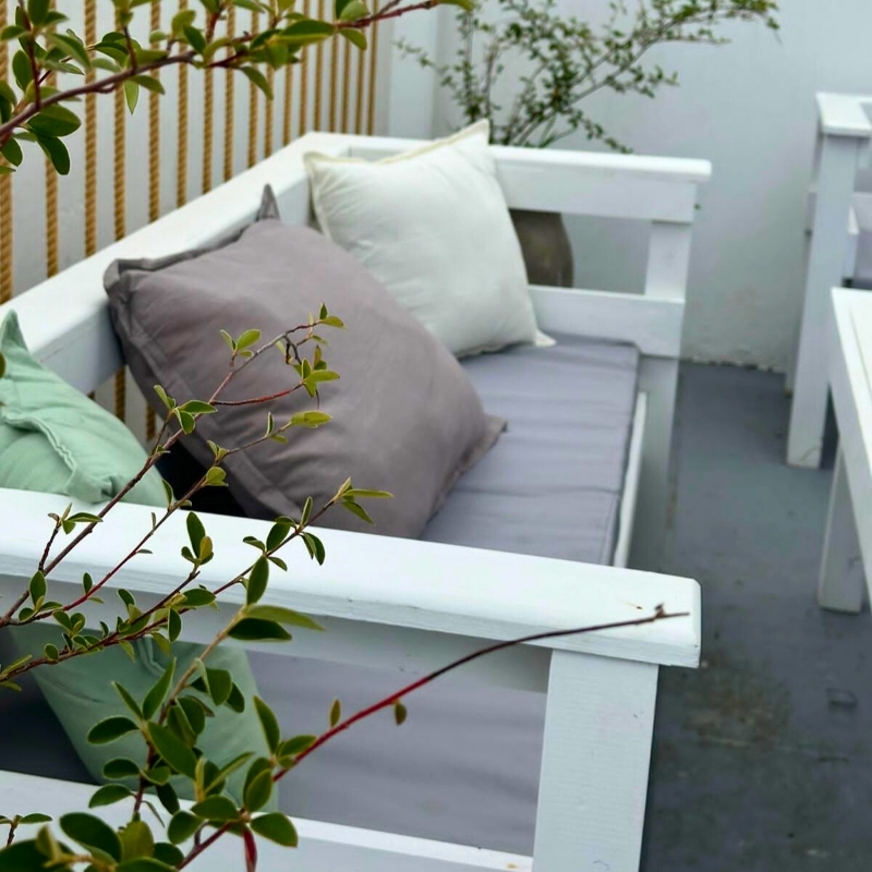 Sillón de madera blanco con almohadones grises y verdes en un balcón
