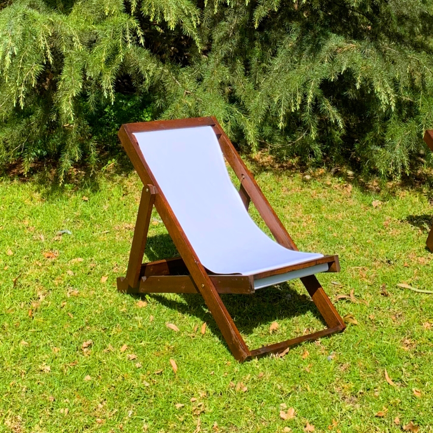 Tumbona plegable de madera con lona blanca sobre el césped