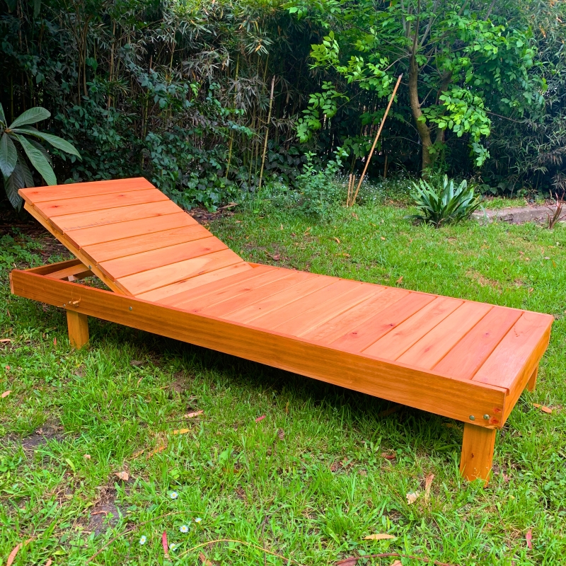 Camastro de madera clara con respaldo reclinable en un jardín