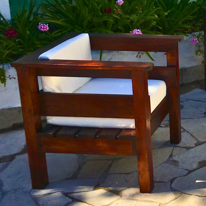 Sillón individual de madera con almohadones blancos en un patio